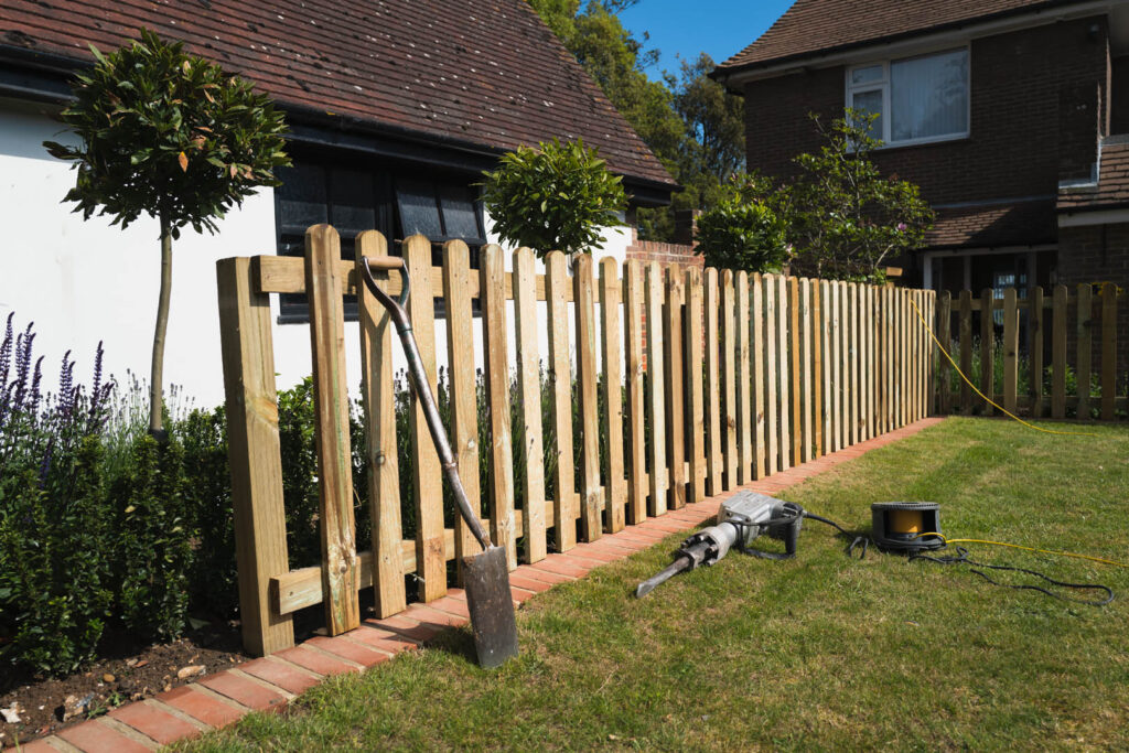 The installation of a wooden, natural wood colour, picket fence in a residential garden.